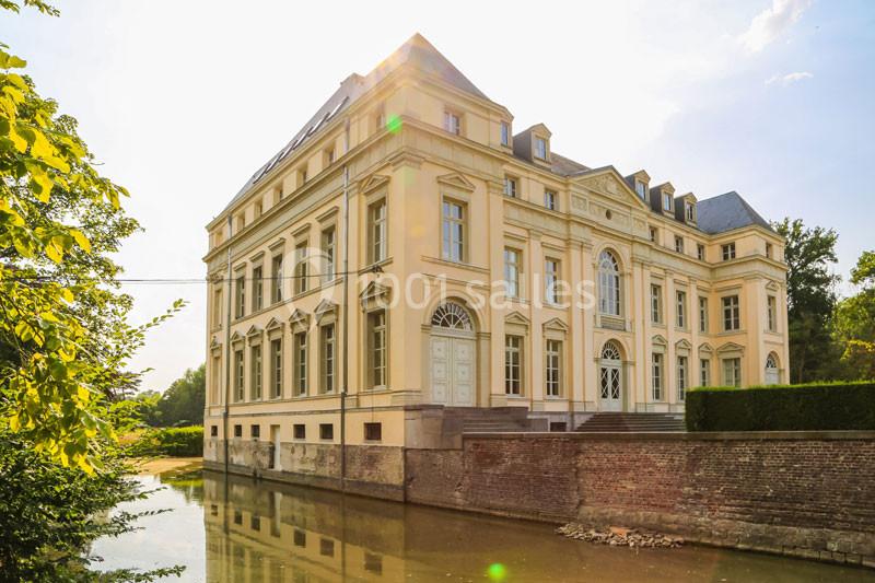 Façade d'un bâtiment classique en pierre claire, bordé par un canal et entouré de végétation.