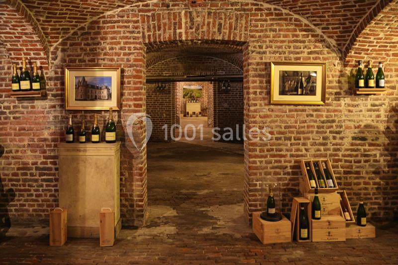 Cave voûtée en briques avec des bouteilles de vin exposées sur des étagères et des caisses en bois.