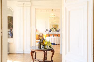 Salon lumineux avec parquet, mobilier classique, table ronde dressée au centre et lustre en cristal au plafond.