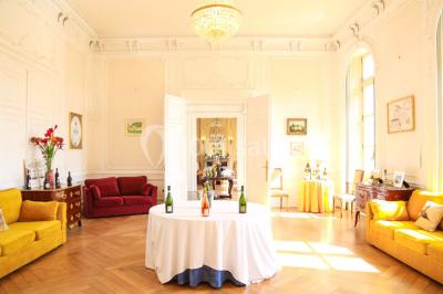 Salon lumineux avec parquet, mobilier classique, table ronde dressée au centre et lustre en cristal au plafond.