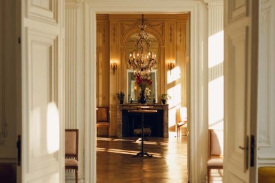 Salon lumineux avec parquet, mobilier classique, table ronde dressée au centre et lustre en cristal au plafond.