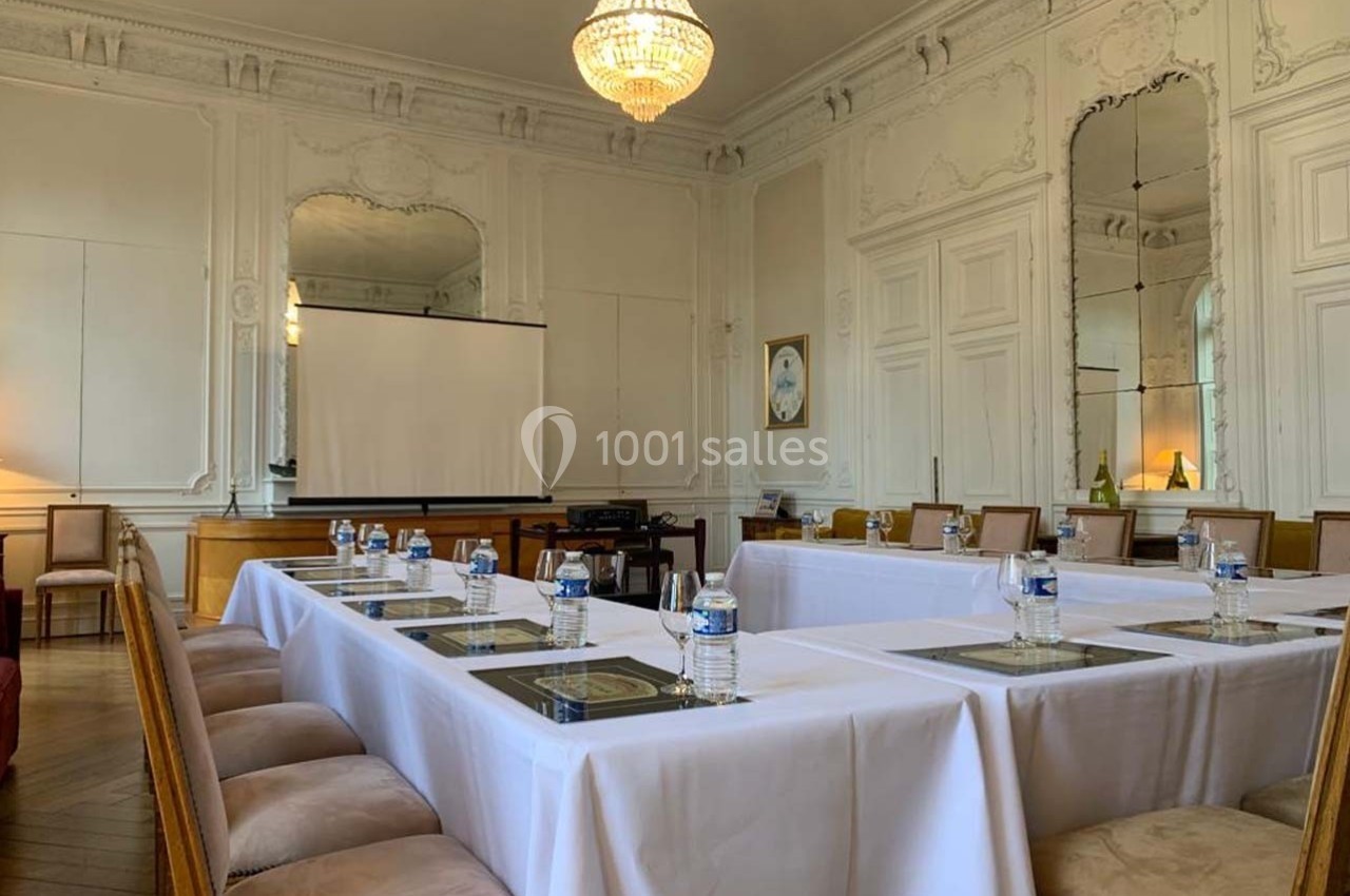 Salle de réunion élégante avec tables disposées en U, chaises rembourrées, écran de projection et décor classique.