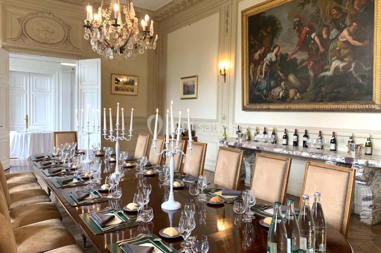 Salle à manger élégante avec une grande table dressée, chandeliers, tableau mural et décor classique.