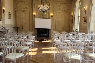 Salon lumineux avec parquet, mobilier classique, table ronde dressée au centre et lustre en cristal au plafond.