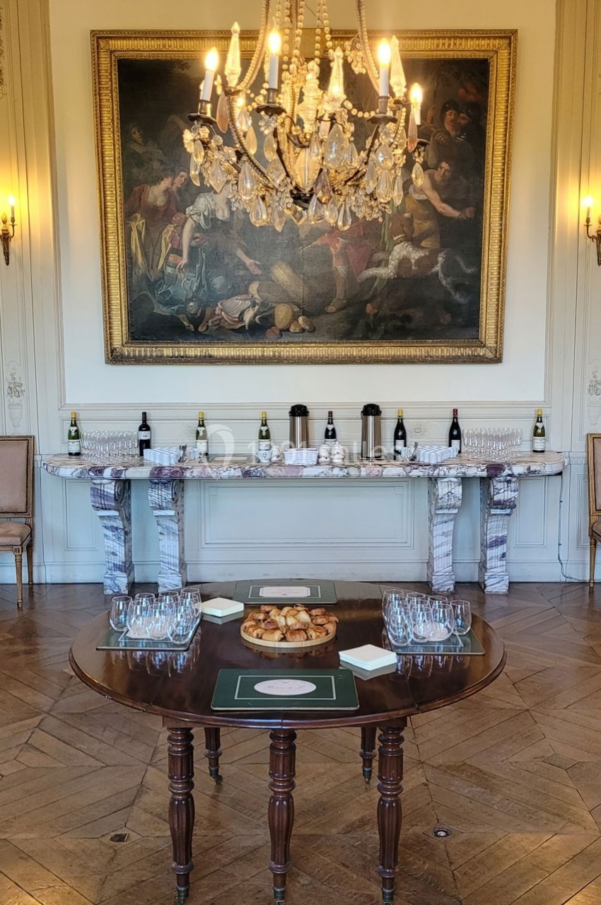 Table dressée avec des verres et des amuse-bouches devant une console ornée de bouteilles de vin, dans une salle élégante.