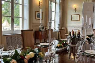 Salon lumineux avec parquet, mobilier classique, table ronde dressée au centre et lustre en cristal au plafond.