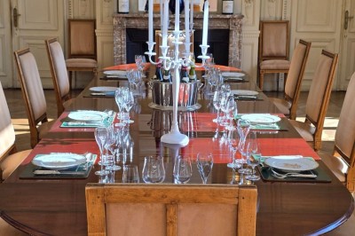 Salon lumineux avec parquet, mobilier classique, table ronde dressée au centre et lustre en cristal au plafond.