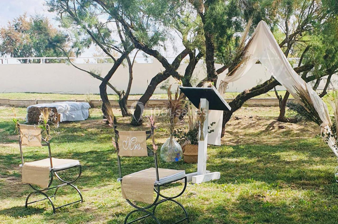 Location salle Arles (Bouches-du-Rhône) - Manade Allard #9 Chaises décorées et pupitre installés en extérieur sous des arbres, avec un voile suspendu en arrière-plan.