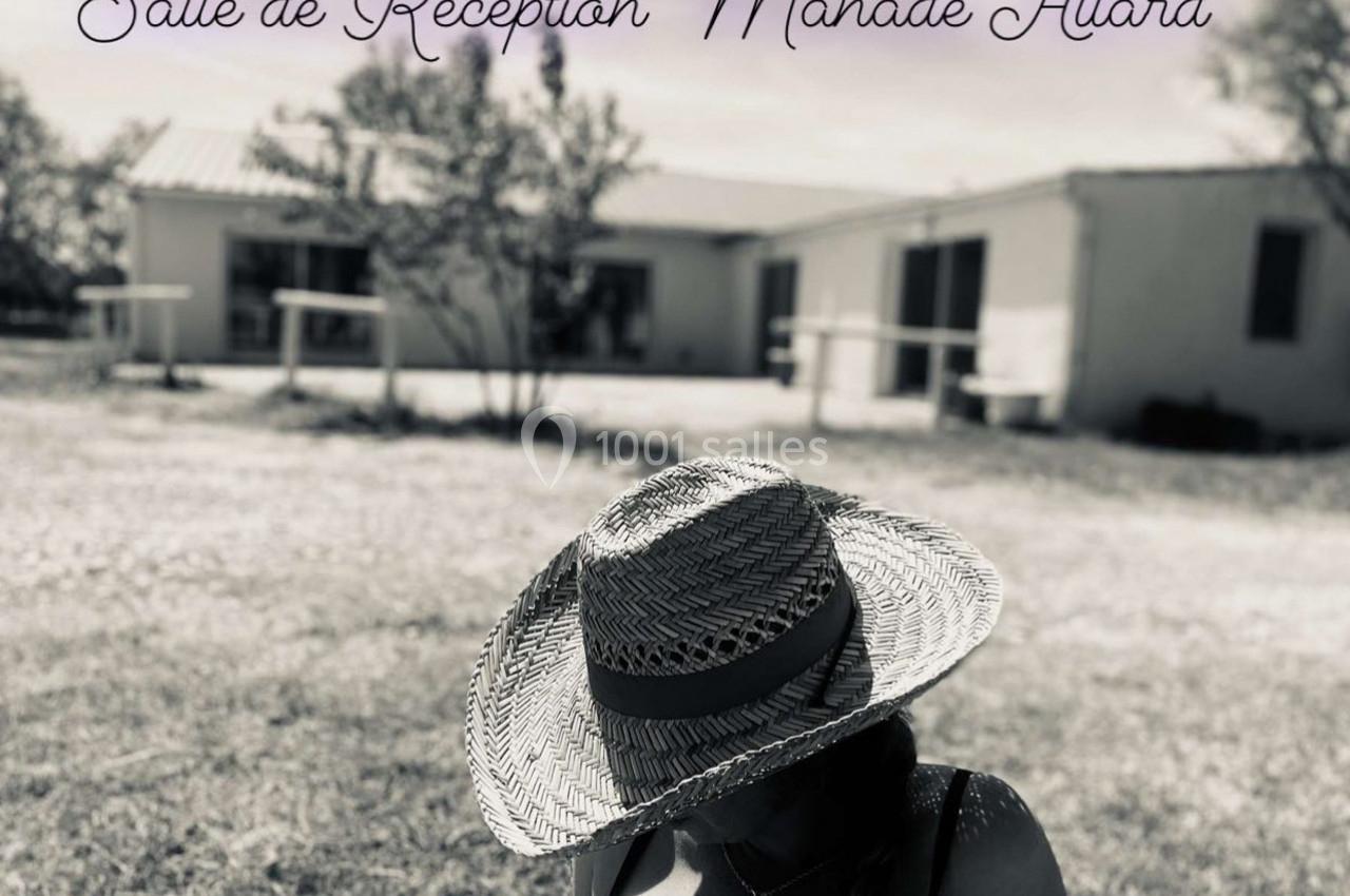 Location salle Arles (Bouches-du-Rhône) - Manade Allard #2 Femme portant un chapeau en paille au premier plan, bâtiment blanc et arbres flous en arrière-plan.