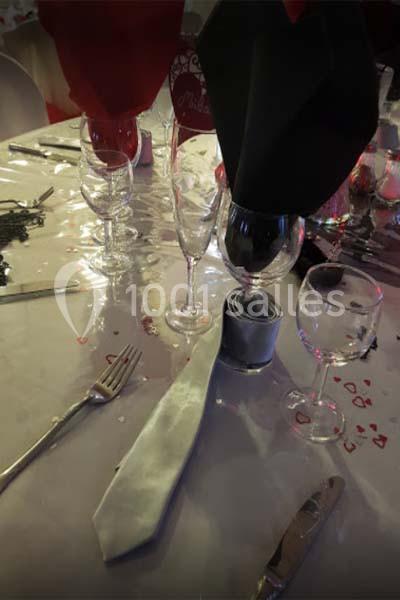Table dressée avec nappe blanche, couverts, verres et serviettes pliées, décorée de confettis en forme de cœur.