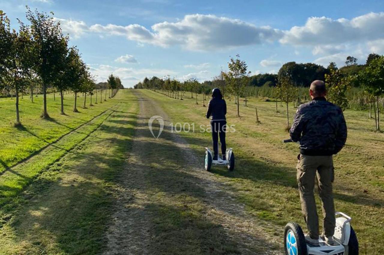 Deux personnes circulent sur des gyropodes le long d'un chemin bordé d'arbres sous un ciel dégagé.