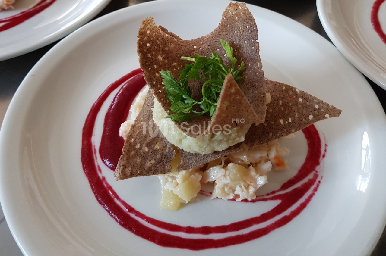 Assiette gastronomique avec tartare de poisson, chips croustillantes, purée et sauce rouge en décoration.