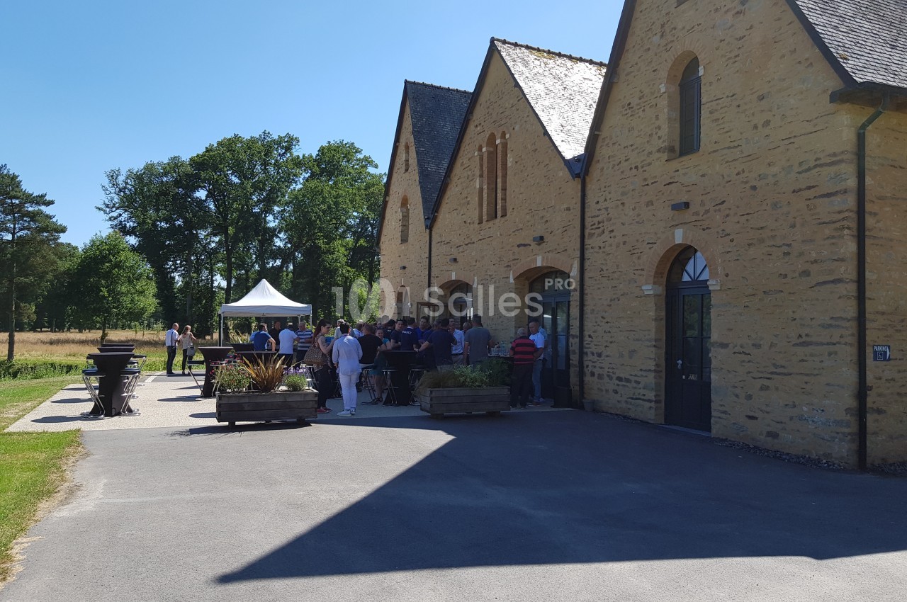 Un groupe de personnes rassemblées devant un bâtiment en pierre sous un ciel ensoleillé.