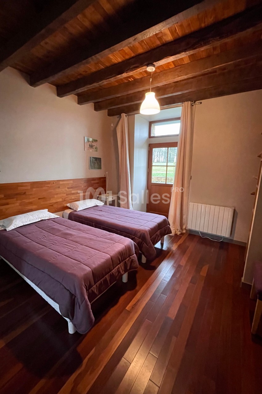 Chambre avec deux lits simples, parquet en bois, plafond avec poutres apparentes et fenêtre donnant sur l'extérieur.