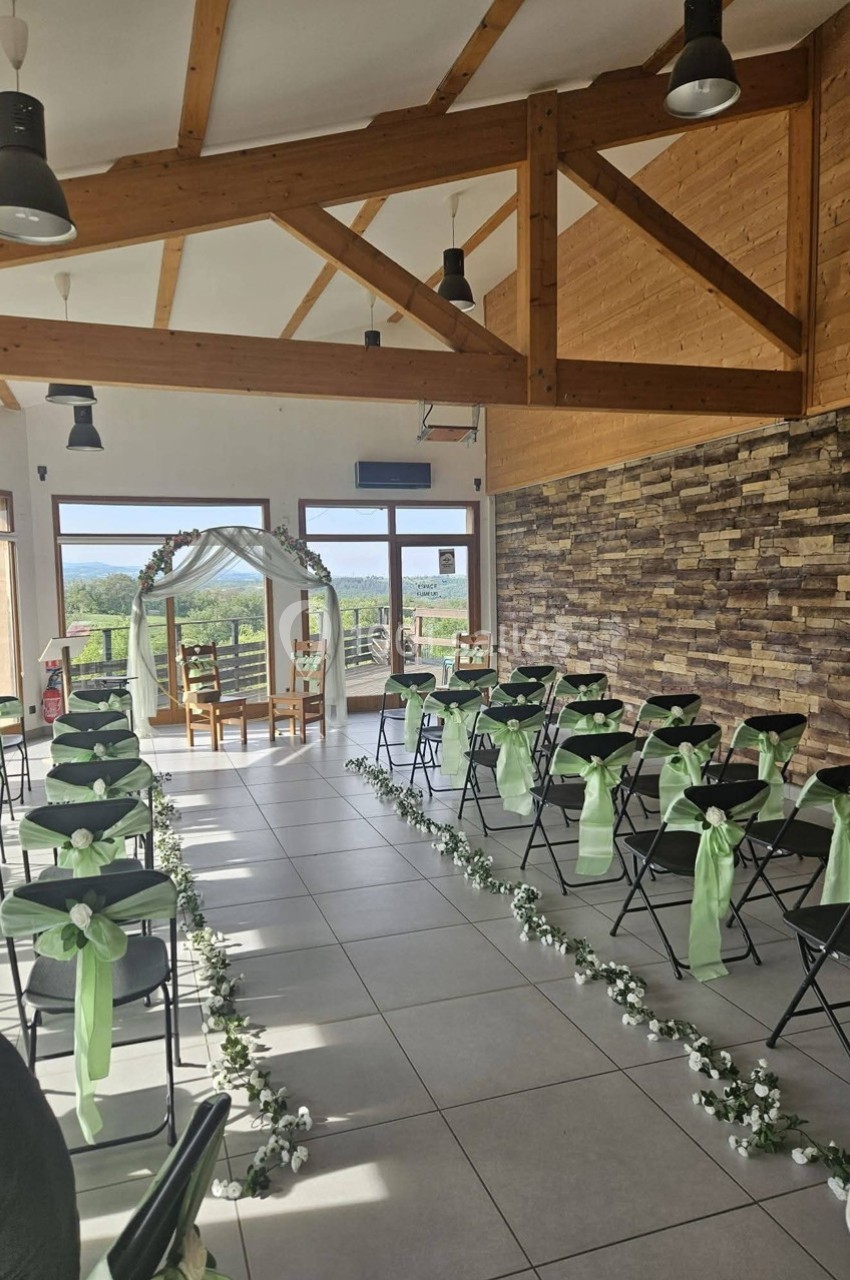 Salle de cérémonie décorée avec des chaises ornées de rubans verts, allée centrale fleurie et arche en arrière-plan.