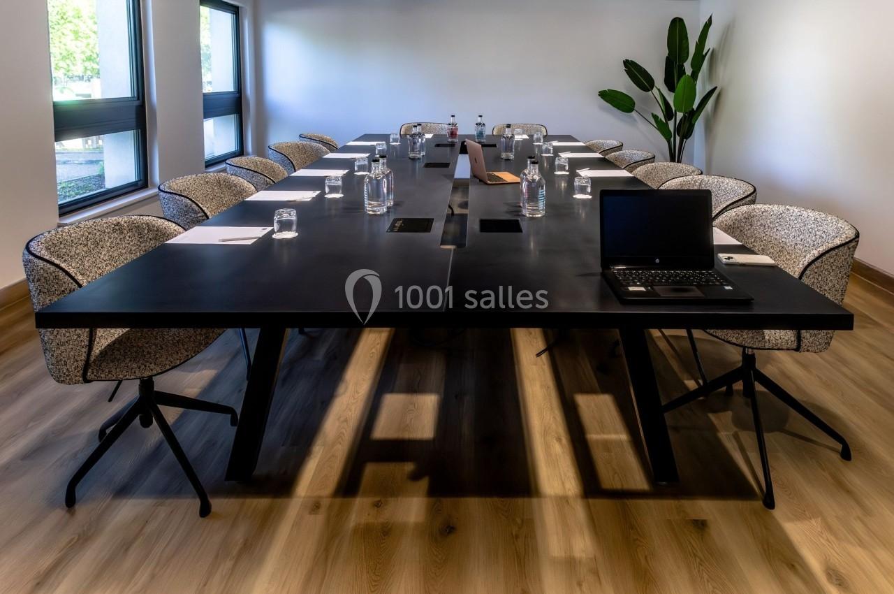 Salle de réunion moderne avec une grande table noire, des chaises rembourrées, des bouteilles d'eau et un ordinateur…