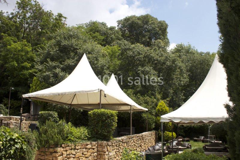 Deux grandes tentes blanches installées dans un jardin verdoyant entouré de murs en pierre.