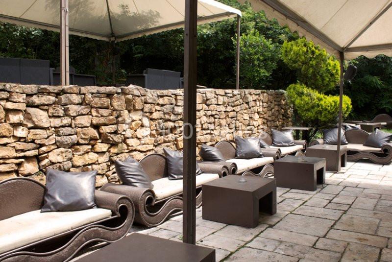 Terrasse aménagée avec des canapés et tables basses, entourée d'un mur en pierre et de végétation.