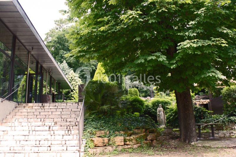 Escalier en pierre menant à un bâtiment vitré, entouré de verdure et d'une statue dans un jardin.