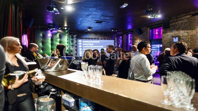 Groupe de personnes échangeant dans un bar ou une salle de réception, avec des lumières tamisées et un comptoir au premier…