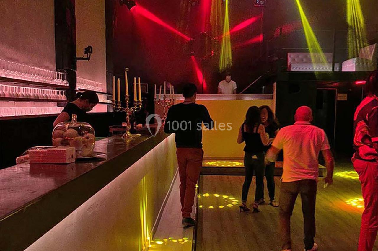 Intérieur d'une discothèque avec bar éclairé, lumières rouges et jaunes, et quelques personnes dansant ou discutant.