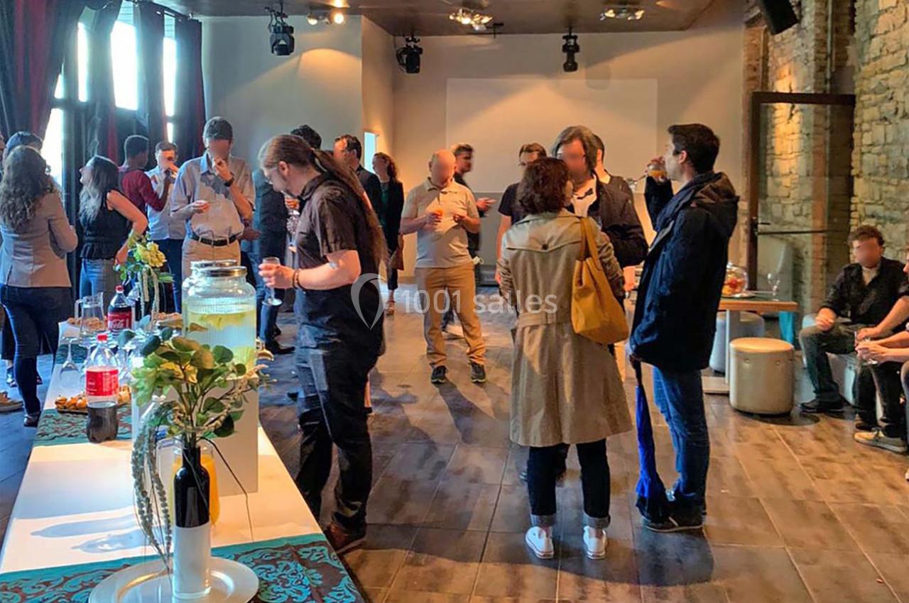 Groupe de personnes discutant dans une salle lumineuse avec des tables de boissons et un mur en pierre.