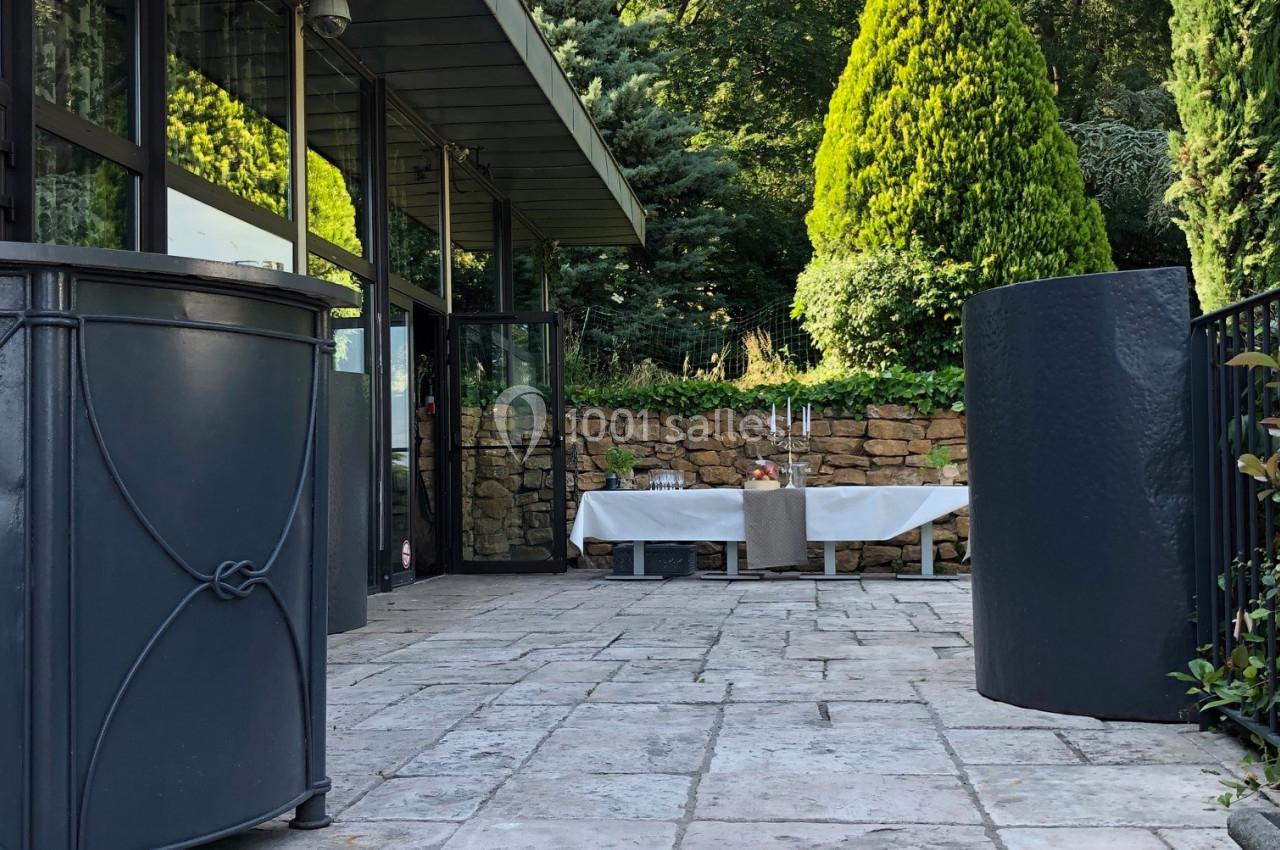 Terrasse en pierre avec table dressée, entourée de verdure et d'une façade vitrée moderne.