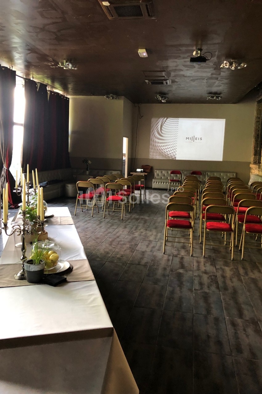 Salle aménagée avec des chaises alignées face à un écran de projection, table dressée en premier plan.