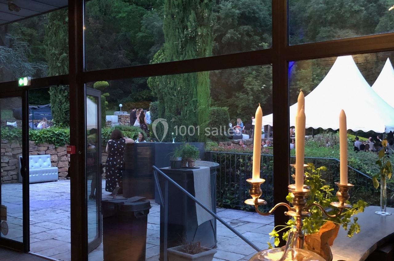 Vue sur un jardin avec des arbres et une tente blanche, depuis une pièce vitrée éclairée, avec un centre de table aux pommes.