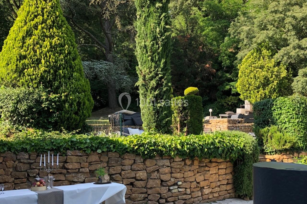 Terrasse en pierre avec tables dressées, bordée de murs en pierre et entourée de végétation dense et arbres.