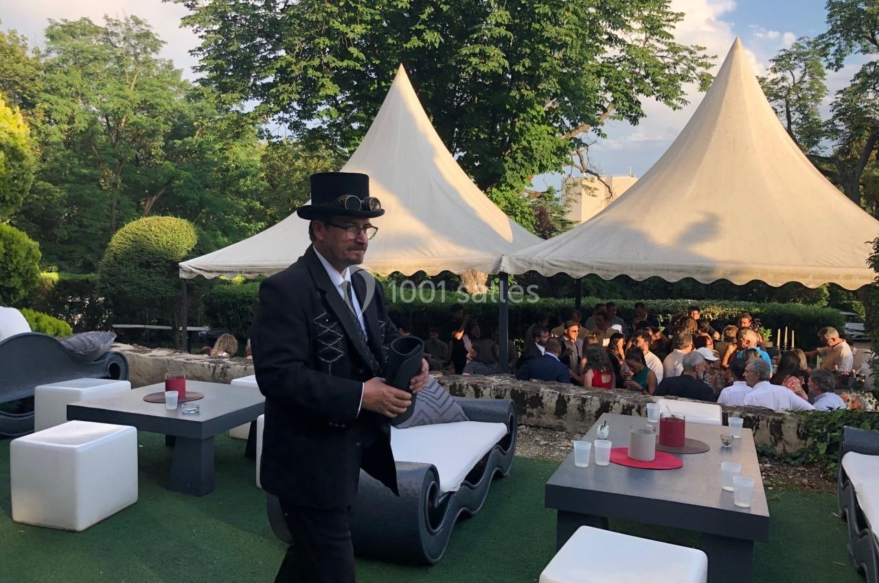 Un homme en costume noir et chapeau haut-de-forme marche dans un espace extérieur avec des tables et des tentes blanches.