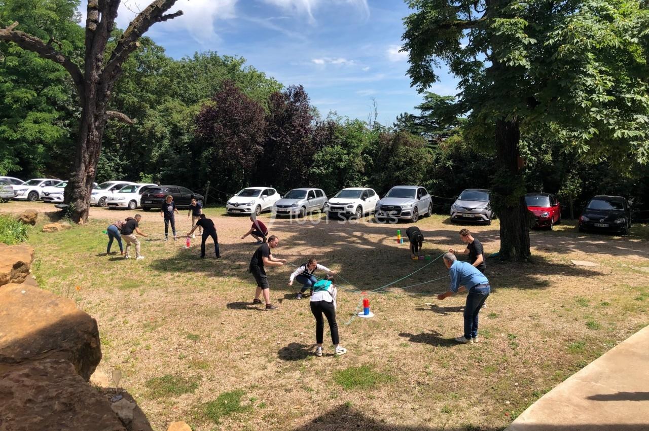Personnes jouant à un jeu en plein air sur une pelouse, entourées d'arbres et de voitures garées en arrière-plan.