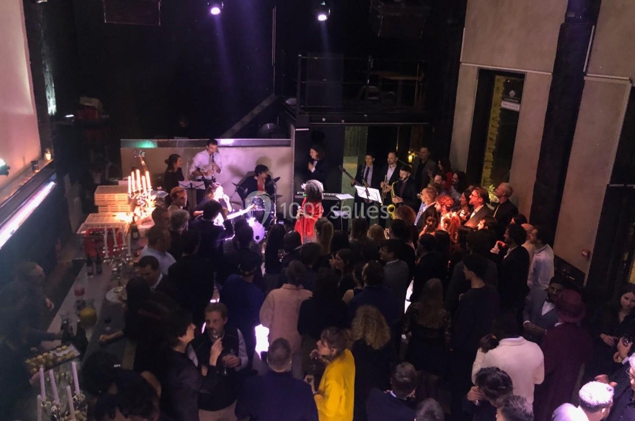 Groupe de personnes rassemblées dans une salle sombre avec un groupe de musiciens jouant sur une scène.