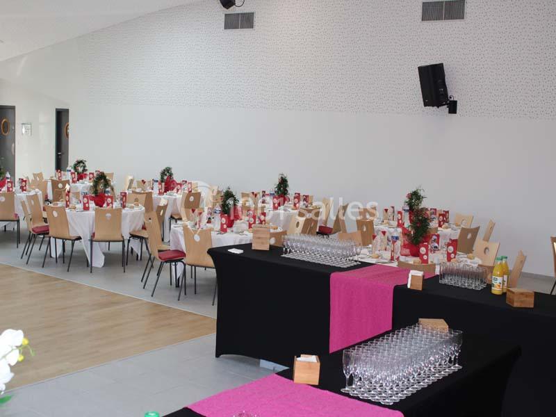 Salle de réception décorée avec des tables dressées, nappes blanches, chaises en bois et verres alignés sur des buffets.