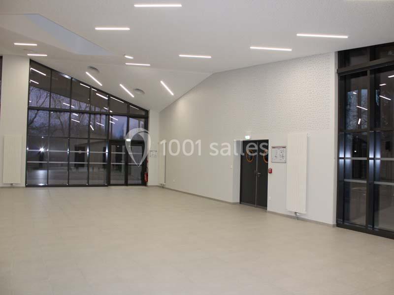 Salle intérieure spacieuse avec de grandes baies vitrées, un sol carrelé clair et un éclairage encastré au plafond.