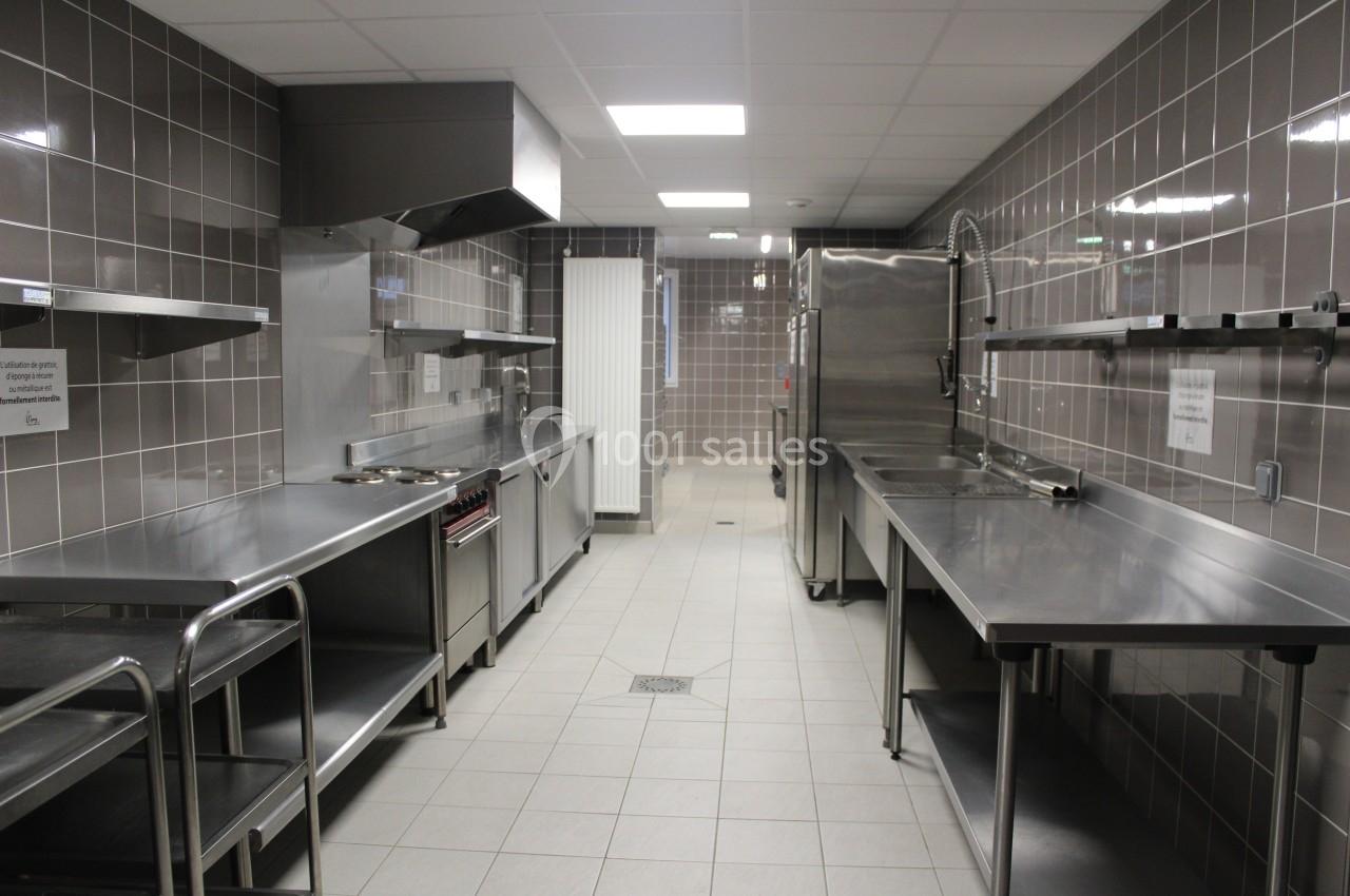 Cuisine professionnelle avec plans de travail en inox, équipements de cuisson, éviers et carrelage mural gris.