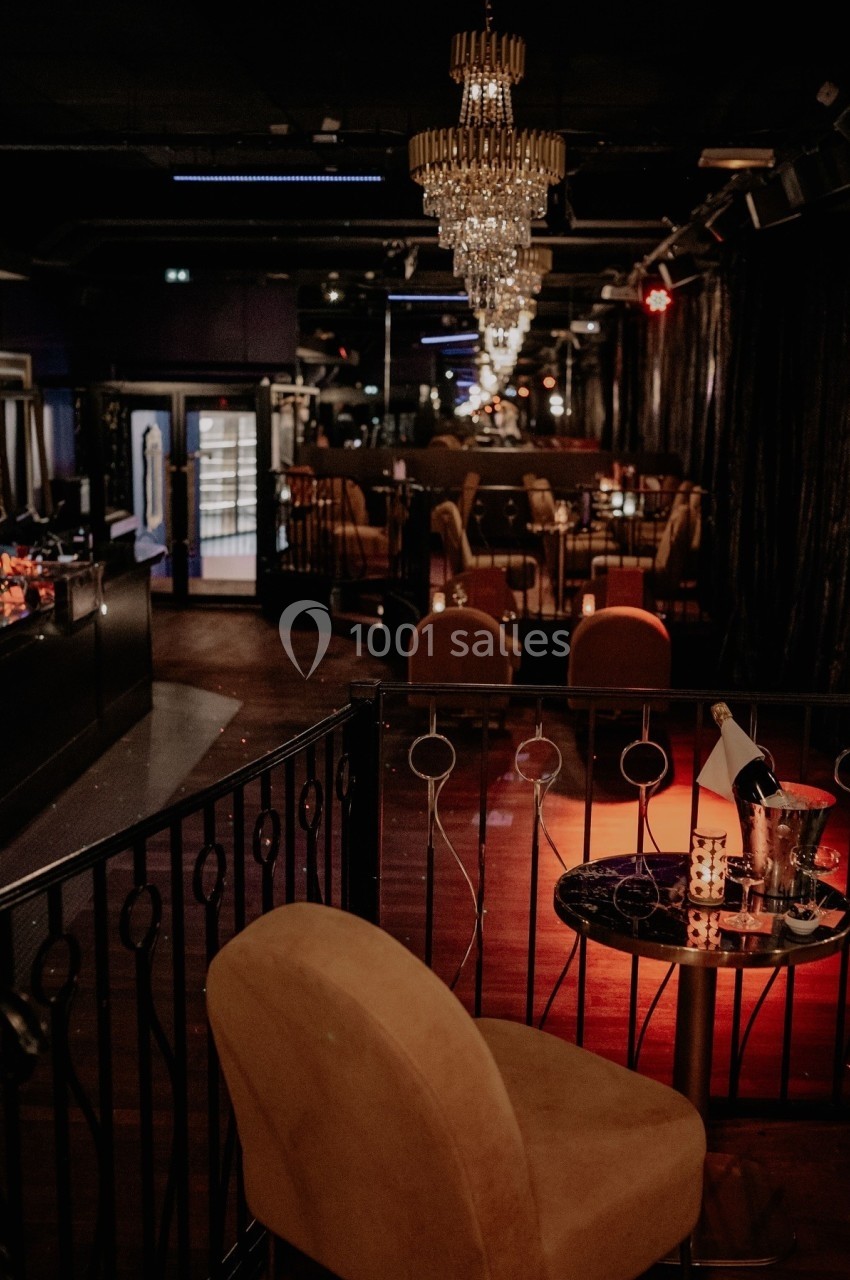 Intérieur d'un bar lounge avec éclairage tamisé, chandeliers suspendus et table avec bouteille et verre.