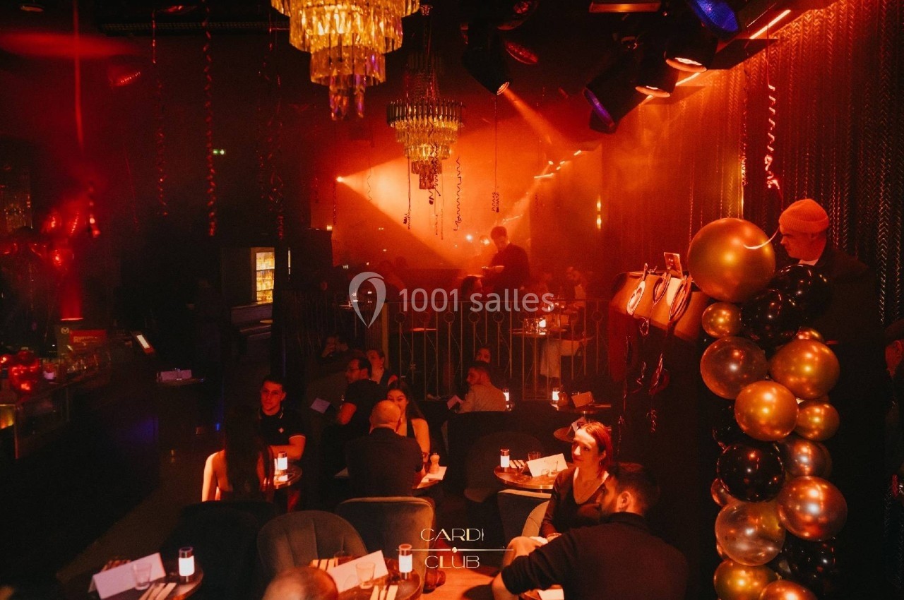 Salle de club avec éclairage tamisé, décorations de ballons et invités assis autour de tables.