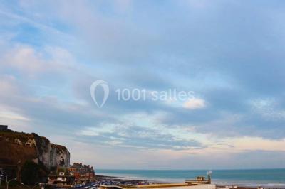 Vue d'une côte avec des falaises, des bâtiments en bord de mer et un ciel partiellement nuageux au crépuscule.