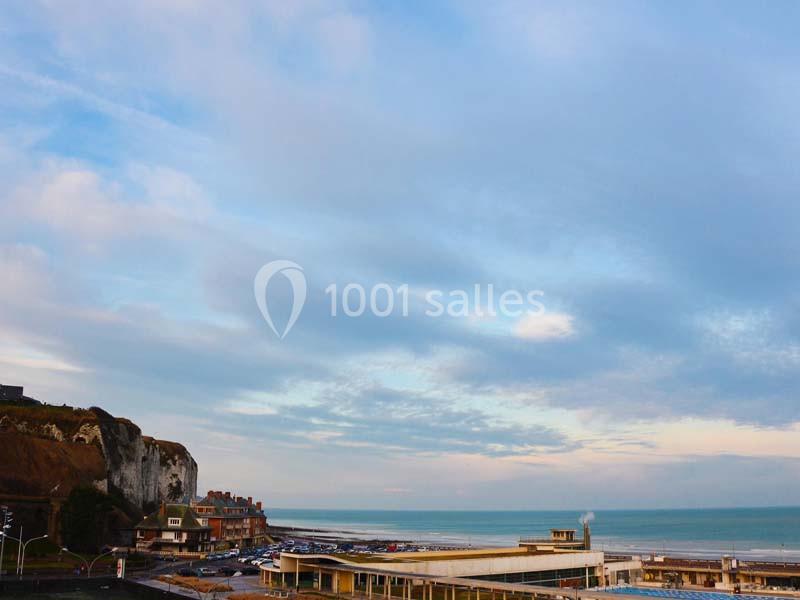 Vue d'une côte avec des falaises, des bâtiments en bord de mer et un ciel partiellement nuageux au crépuscule.