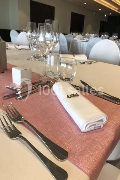 Table dressée avec nappe rose, couverts en métal, verres à pied et serviette blanche ornée du mot ’Love’.