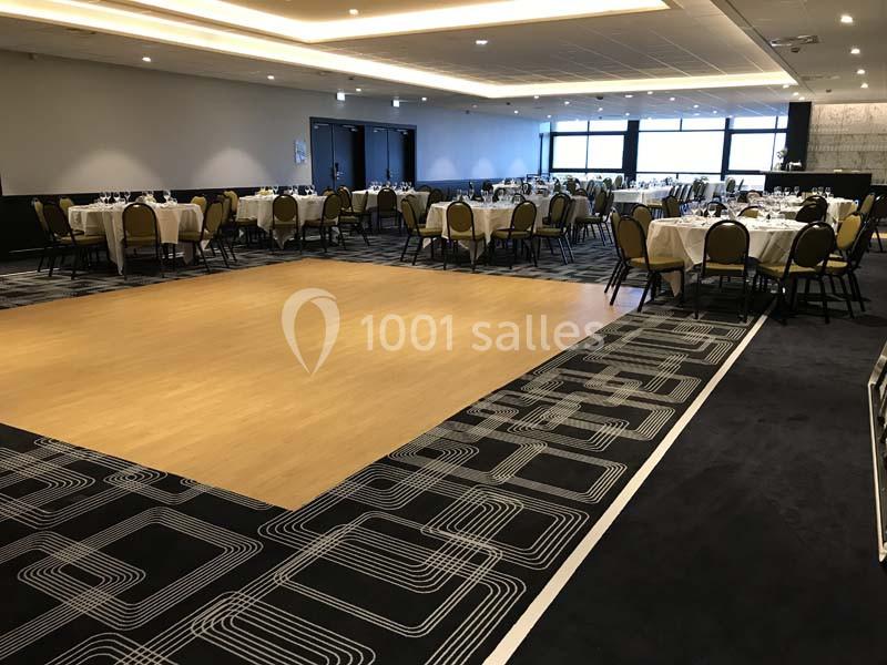 Salle de réception avec tables dressées et piste de danse en bois au centre, éclairée par des lumières artificielles.