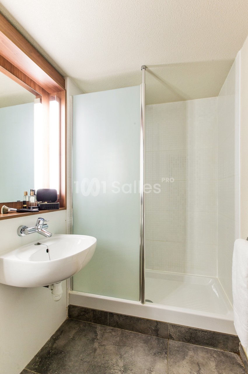 Salle de bain avec douche à paroi vitrée, lavabo suspendu, miroir éclairé et sol en carrelage foncé.