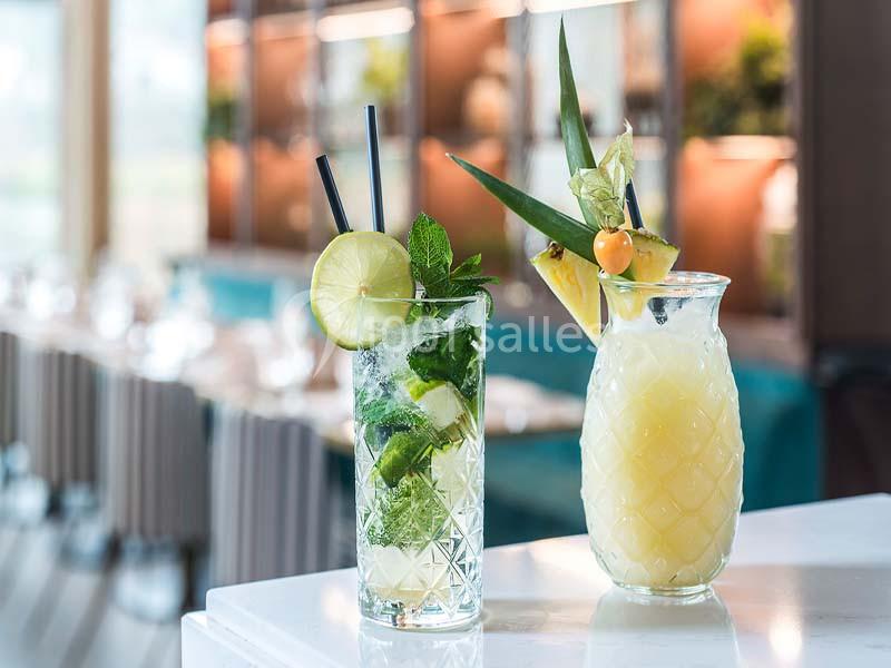 Deux verres de cocktails, l'un avec menthe et citron vert, l'autre à base d'ananas, posés sur une table blanche.