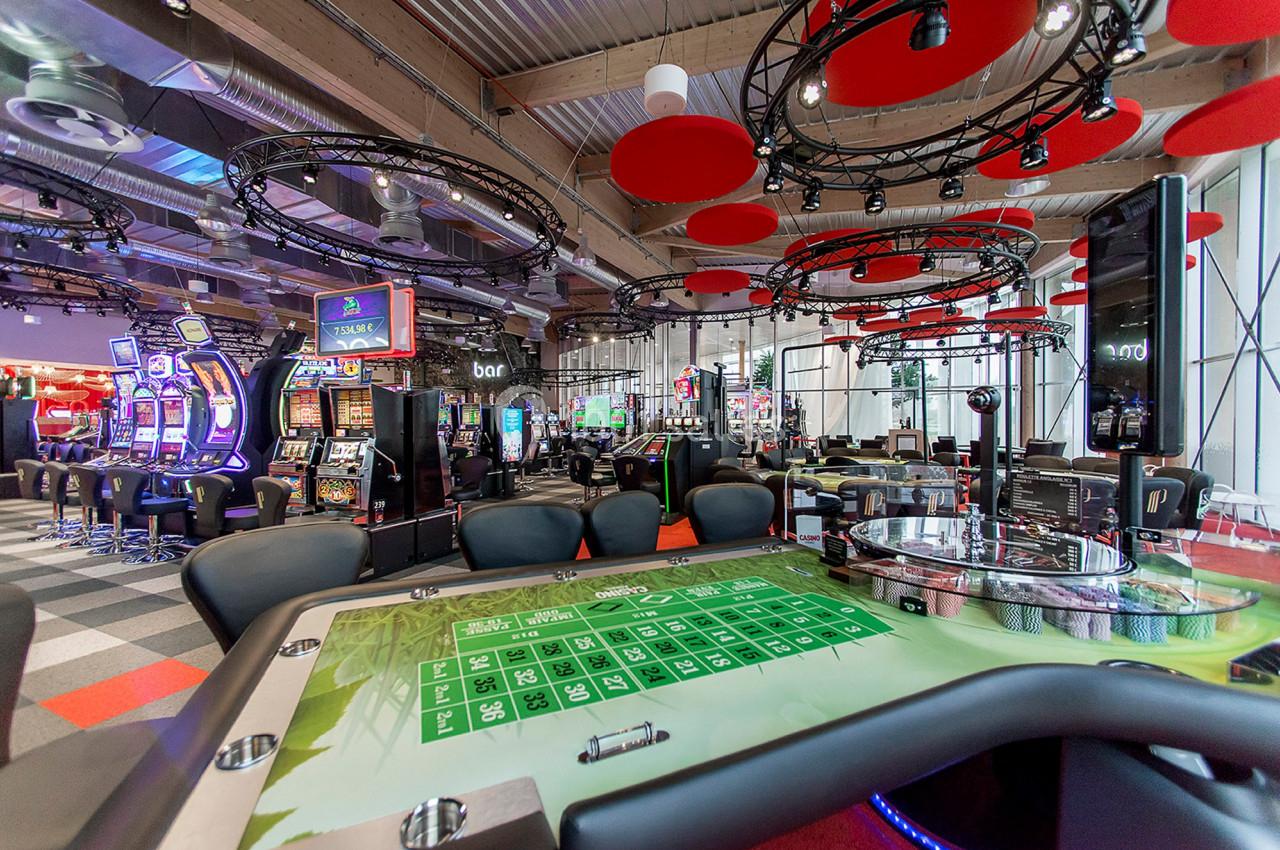 Salle de casino moderne avec tables de jeux, machines à sous et décorations suspendues rouges.