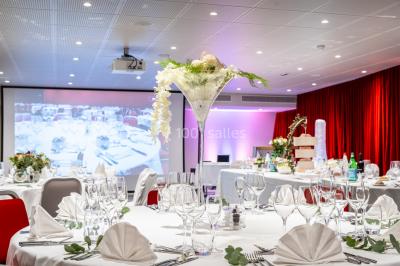 Bâtiment moderne en bord de rivière, entouré de verdure, avec un pont piétonnier au premier plan.