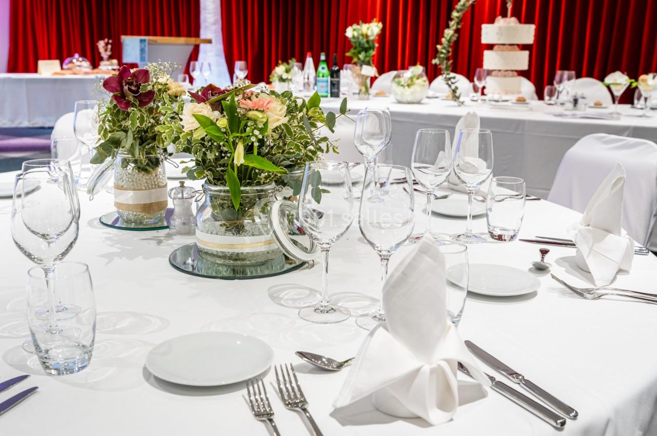 Table élégamment dressée avec nappes blanches, verres, couverts, serviettes pliées et centre de table floral.