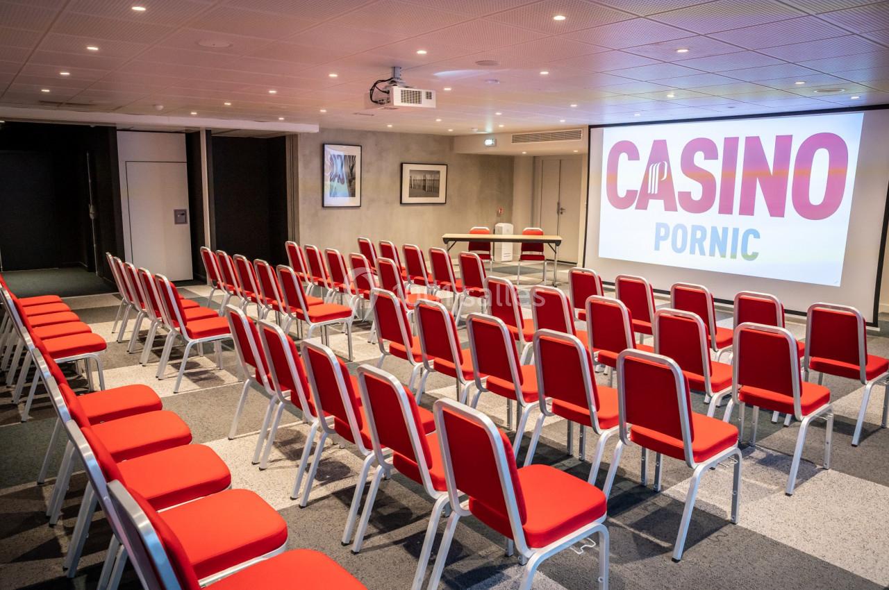 Salle de conférence avec des rangées de chaises rouges alignées face à un écran affichant ’Casino Pornic’.