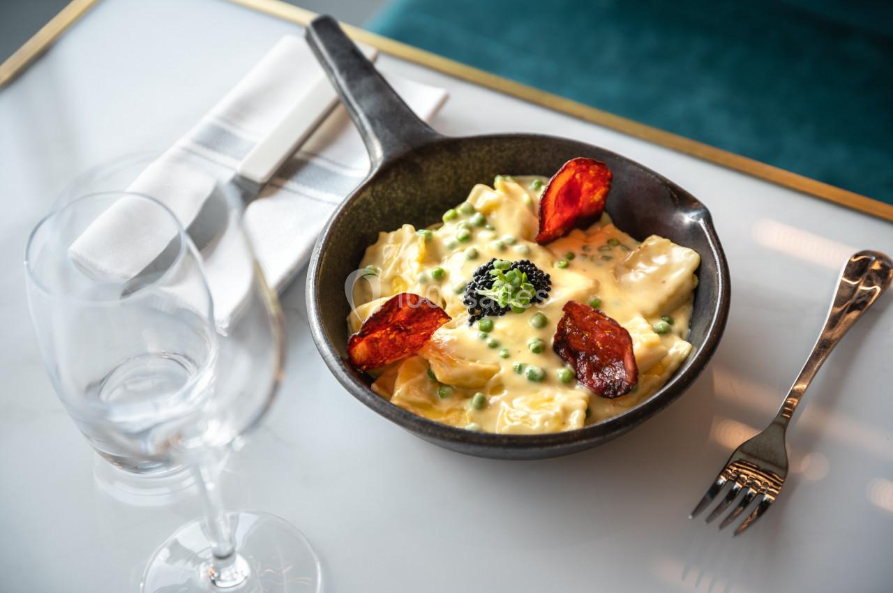 Assiette de raviolis à la sauce crémeuse, garnis de petits pois, brocoli, chorizo et caviar, sur une table élégante.