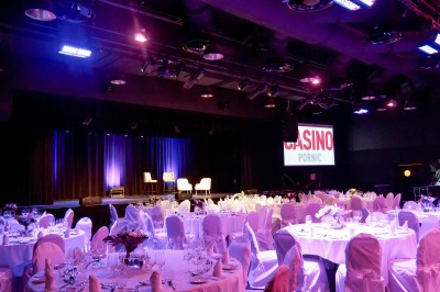 Bâtiment moderne en bord de rivière, entouré de verdure, avec un pont piétonnier au premier plan.